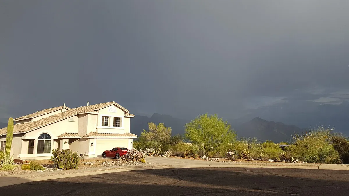 A two-story stucco house in Oro Valley under a dark monsoon storm cloud