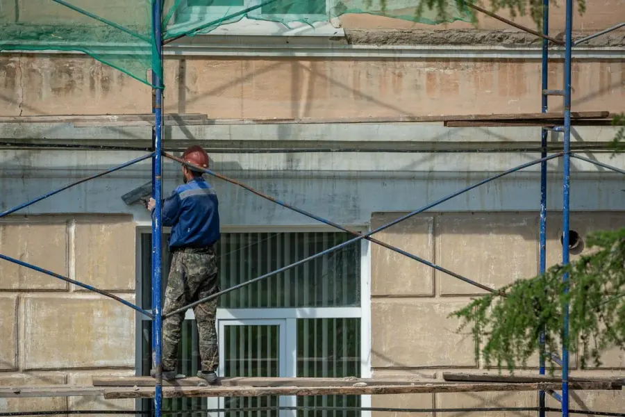 Contractor on scaffolding coating an upper-story exterior wall, the access condition that adds 10 to 20 percent to a Tucson stucco or EIFS bid