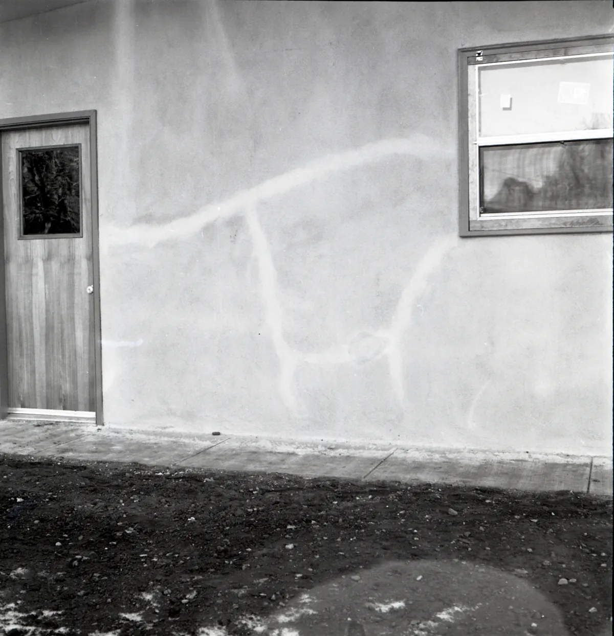 Stucco repair around windows: black and white photo of cracks running across a stucco wall between a door and a window